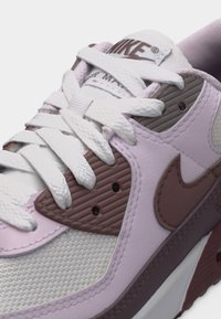 Detailný záber bielej a fialovej tenisky Nike s textúrovanými panelmi, bielymi šnúrkami a logom Nike z boku.