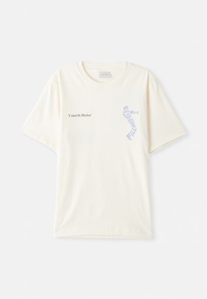 T-shirt en coton blanc à manches courtes, présentant le texte « United By Rhythm » en noir et bleu sur la poitrine. Design à col rond.