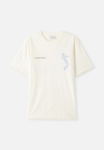 T-shirt en coton blanc à manches courtes, présentant le texte « United By Rhythm » en noir et bleu sur la poitrine. Design à col rond.