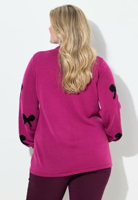 Magenta sweter z długimi rękawami, ozdobionymi czarnymi kokardkami, z prążkowanymi mankietami i luźnym krojem. Miękka, dziana tekstura, gładkie wykończenie.