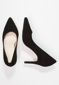 Chaussures à talons hauts en daim noir avec un bout pointu et un talon aiguille de 7,5 cm. L'intérieur présente une doublure beige lisse.