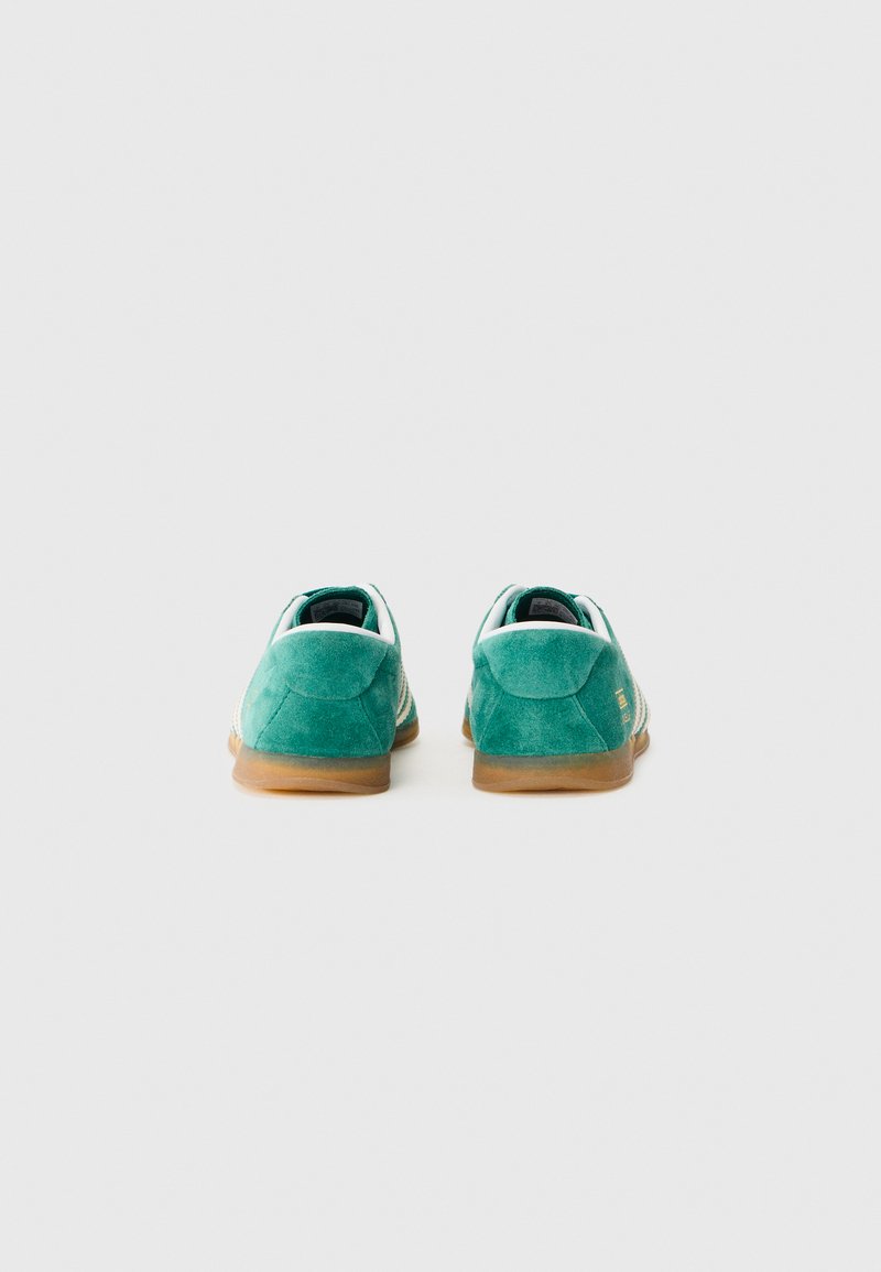 Grønne ruskinds sneakers med en gummisål, der har hvide accenter langs kanterne og et struktureret bagpaneldesign. Bageste visning vist.