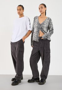 White oversized t-shirt with flame print, gray corduroy cargo pants, and black lace-up boots. Leopard print cardigan with a cropped fit.