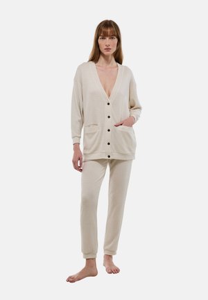 Ensemble de détente en tricot beige comprenant un long cardigan avec un décolleté en V et des boutons, associé à un pantalon fuselé, tous deux avec des poches avant.