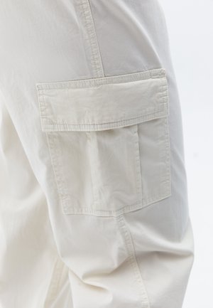 Pantaloni cargo beige con una texture morbida, caratterizzati da una grande tasca laterale e cuciture dettagliate. Il tessuto appare leggero e resistente.