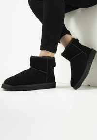 Zwarte suède enkelboots met een zachte bontvoering, vlakke rubbere zool en gestikte accenten. Heeft een ronde neus en een achterste tab voor gemakkelijk aan- en uittrekken.