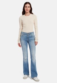 Maglia a maniche lunghe di un beige chiaro texturizzato abbinata a jeans flared azzurri con dettagli strappati e sneakers bianche.