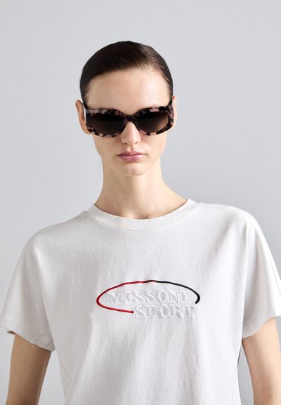 Skildpaddemønstrede solbriller med en markant rektangulær form, mørke linser og en blank finish, parret med en hvid T-shirt med rund hals og broderet tekst.
