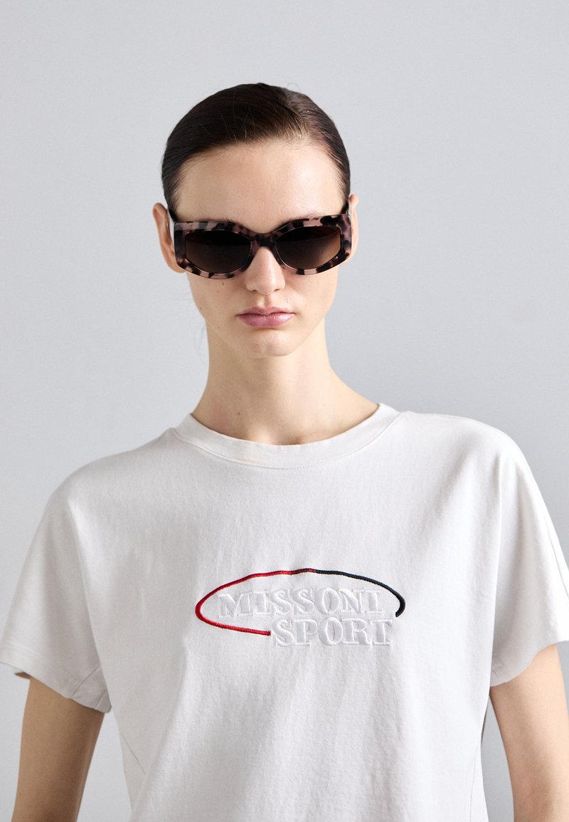 Γυαλιά ηλίου καβουριού με έντονο ορθογώνιο σχήμα, σκούρους φακούς και γυαλιστερή φινίρισμα, συνδυασμένα με λευκό μπλουζάκι τύπου crew neck που διαθέτει κεντημένο κείμενο.