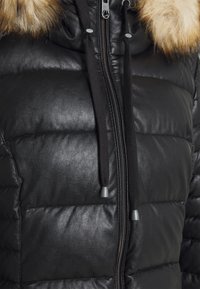 Schwarze gepolsterte Lederjacke mit einer Kapuze aus Kunstpelz, Kordelzügen und silbernen Hardware-Details, mit einer glatten, strukturierten Oberfläche.