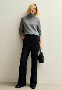 Grå polotröja med långa ärmar, tillsammans med högmidjade mörk denim vida byxor. Svart handväska som tillbehör.