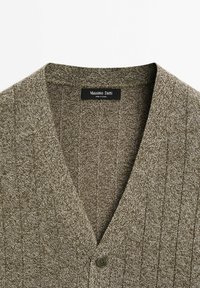 Brun stickad cardigan med V-ringad design, som har vertikal ribbad textur och en enda knappstängning. Märkesetikett synlig inuti.