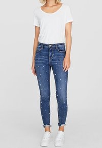 Mörkblå skinny jeans i denim med pärlprydnader och fransade fållar, kombinerat med en vit t-shirt med kort ärm och vita sneakers.