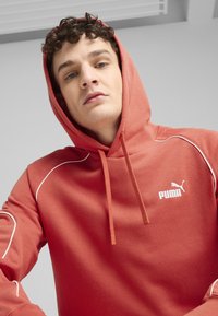 Rdeča kapuca iz mehkega materiala z belimi detajli, ki ima sprednji kenguru žep, nastavljivo kapuco s vrvico in logo Puma.