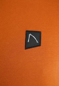 Un tessuto arancione con una texture liscia presenta un patch quadrato nero che mostra un semplice design geometrico bianco.