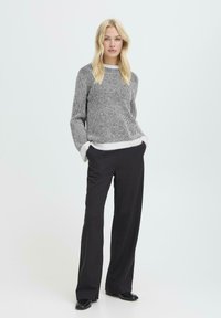 Hallikate ja valged triibudega sviiter, ümar kaelus ja laiad varrukad, kombineeritud mustade laienevate pükstega ja mustade kingadega. Lihtne ja moderna disain.