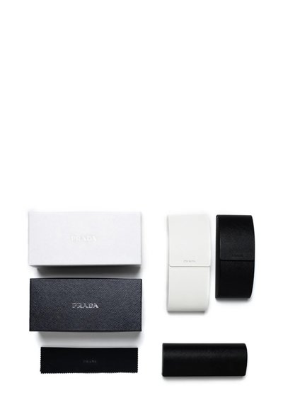 Il packaging Prada include una scatola bianca, due scatole nere e un astuccio per occhiali bianco e nero, caratterizzati da superfici testurizzate con dettagli del logo.