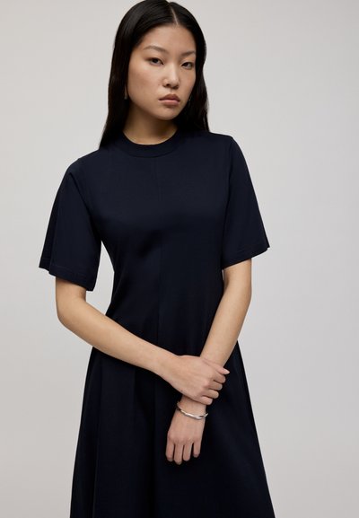 Granatowa sukienka z krótkim rękawem, okrągłym dekoltem, gładkiego materiału i prostym kroju; zawiera subtelne detale szwów.