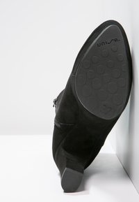 Black suede ankle boot with a zip closure, low heel, and patterned rubber outsole, displaying size 37 on the bottom.