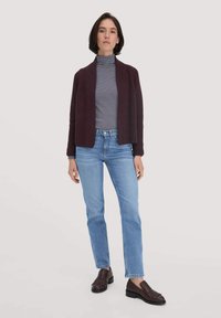 Aubergine Strickjacke über einem navyblauen und weißen gestreiften Rollkragenpullover, hellblaue Jeans und dunkelbraune Loafer mit Fransen.