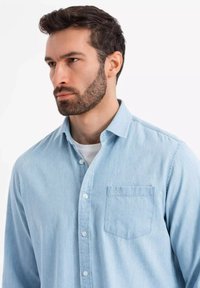 Chemise en denim bleu clair avec col boutonné, dotée d'une poche poitrine unique et d'une finition douce et texturée.