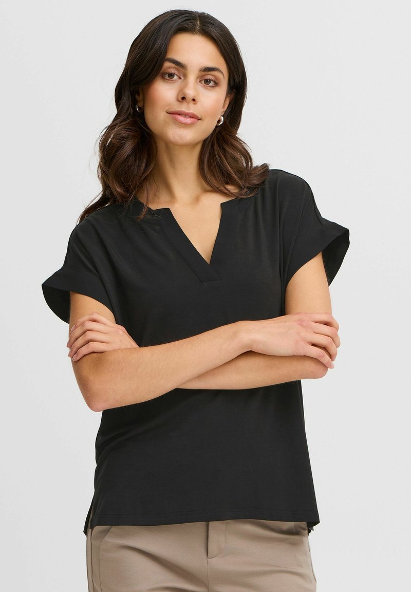 Top nero a maniche corte con scollatura a V, realizzato in materiale morbido. Presenta maniche arrotolate e spacchi laterali sull'orlo, offrendo una vestibilità rilassata.