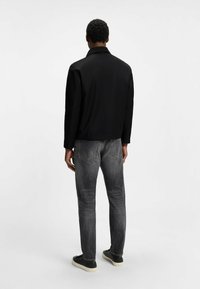 Schwarze Jacke mit Kragen, kombiniert mit dunkelgrauen Jeans. Das Set zeichnet sich durch eine glatte Textur und eine moderne Passform aus, mit minimalistischen Details.