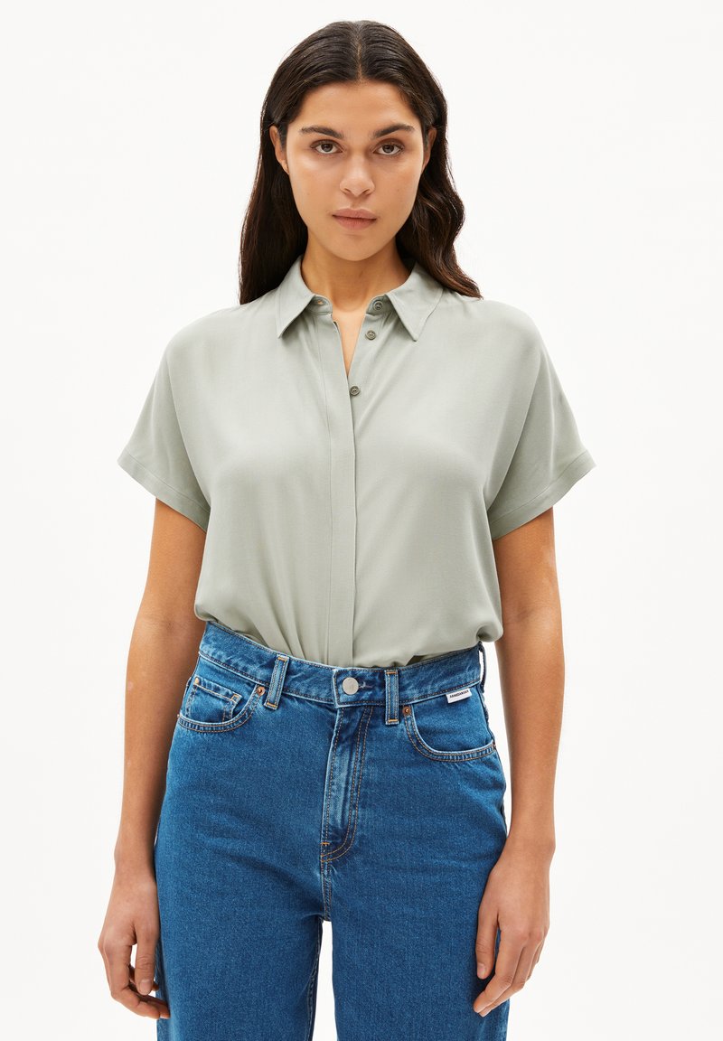 Lichtgroene blouse met korte mouwen, een kraag en knoopsluiting, gecombineerd met high-waisted blauwe jeans. Gladde textuur.