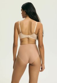 Kobieta z długimi ciemnymi włosami, ubrana w cieliste majtki z wysokim stanem i pasujący do nich biustonosz, widziana od tyłu na jednolitym jasnym tle.