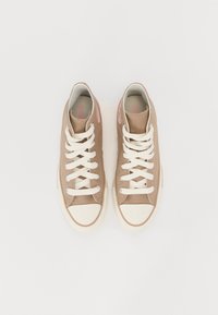 Baskets en toile marron clair avec lacets blancs et bout renforcé blanc, arborant un logo rose sur le côté et une texture lisse. Design classique à tige basse.