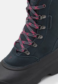 Botte imperméable bleu foncé avec une tige texturée, œillets en métal et lacets roses. Caractérisée par une semelle en caoutchouc noir épaisse et un embout renforcé.