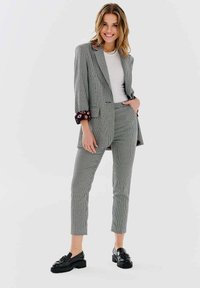 Szary żakiet w kratę z kontrastowymi detalami przy mankietach, w zestawie ze dopasowanymi spodniami. Czarne mokasyny dopełniają stylizację.