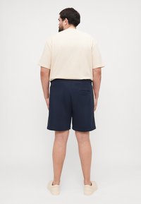 Marina shorts med sidofickor, elastisk midja och en bakficka. Tillsammans med en ljusbeige kortärmad t-shirt. Slät textur.