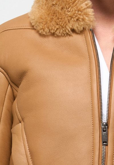 Giacca di pelle color tan con un colletto in shearling beige peloso, caratterizzata da una zip metallica e cuciture strutturate. Texture liscia, vestibilità sartoriale.