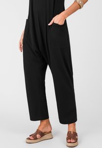 Jumpsuit nero con una forma oversize, dotato di due tasche laterali. Abbinato a sandali con zeppa marroni, che valorizzano sia il comfort che la funzionalit�à.