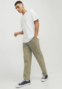 Weißes Baumwoll-T-Shirt mit lockerer Passform, kombiniert mit hellgrünen Hosen und navyblauen Sneakers mit weißen Sohlen. Einfaches, lässiges Outfit mit Taschen.