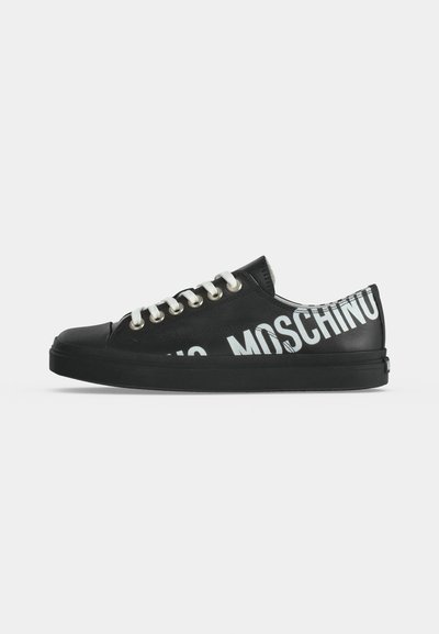 Baskets basses noires avec lacets blancs et grand texte blanc MOSCHINO sur le côté et au talon sur fond uni.