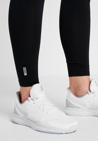 Fötter i vita Nike löparskor och svarta träningstights med en B.DRY-etikett på underbenet.