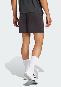 Sorte idrettsshorts med teksturert finish og avslappet passform, kombinert med hvite sokker og hvite sko med svarte detaljer.