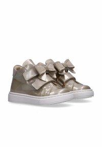 Sneakers in pelle verniciata beige con doppie chiusure in velcro e fiocchi decorativi, dotate di suola in gomma bianca e punta strutturata.