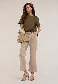 Camiseta de manga corta en verde oliva con bordado de hojas, combinada con pantalones beige de pierna ancha y sandalias de tacón alto con tiras.