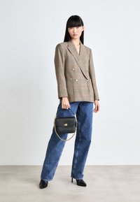 Dubbelknäppt rutigt blazer i beige och bruna nyanser, kombinerad med lösa blå denimjeans. Håller en svart läderhandväska med en guldkedja.