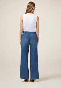 Jeans de mezclilla azul de pierna ancha con cinturilla elástica, dos bolsillos traseros y una textura suave; combinados con una blusa sin mangas blanca.