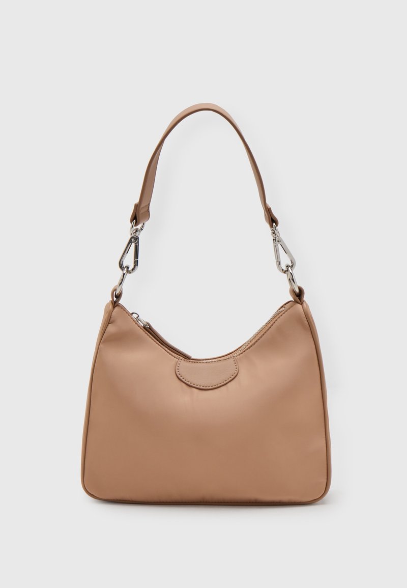 Petit sac à main en cuir beige avec une courte bandoulière attachée par des fermoirs métalliques argentés, sur un fond clair uni.