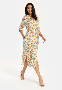 Floral wrap dress featuring a white background with colorful fruit patterns, short sleeves, tie waist, and side slits. Smooth fabric, lightweight.