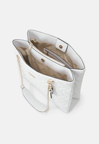 Bílá prošívaná taška přes rameno se zlatým řetízkovým detailem, zapínáním na zip a druky. Uvnitř je béžová podšívka se zeleným logem.