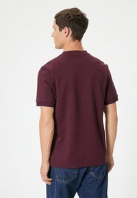 T-shirt in cotone bordeaux con maniche corte, scollo a girocollo a costine e taglio aderente, abbinato a jeans in denim blu.