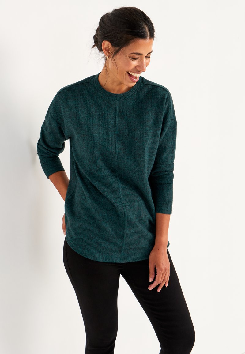 Tannengrüner Strickpullover mit rundem Halsausschnitt, langen Ärmeln und lockerer Passform. Verfügt über ein strukturiertes Muster und seitliche Nähte. Kombiniert mit schwarzen Hosen.