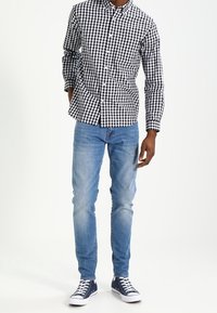 Black and white checked button-up shirt, blue denim jeans, and navy sneakers. Focus on the shirt's fabric and pattern details.