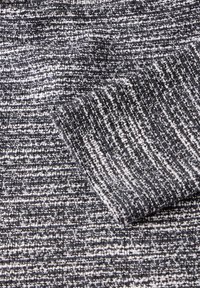 Graues und weißes Textil mit einer strukturierten Oberfläche und einem gewebten Muster, das eine auffällige Manschettenkante aufweist; weich und isoliert im Aussehen.